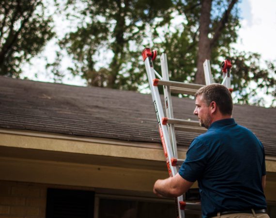 A man climbs a ladder to inspect a roof.